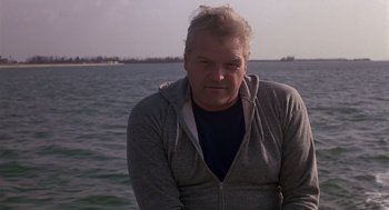 Movie still from “Cocoon” (1985), directed by Ron Howard – A man in a gray jacket standing in front of a body of water; Close Up shot, Low angle