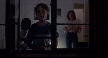 Movie still from “Cocoon” (1985), directed by Ron Howard – A boy standing in front of a window with a woman standing in the background; Medium shot, Over the shoulder angle