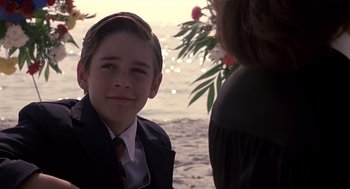 Movie still from “Cocoon” (1985), directed by Ron Howard – A young boy wearing a suit and tie on the beach; Close Up shot, Over the shoulder angle