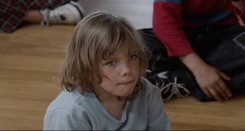Movie still from “Code Unknown” (2000), directed by Michael Haneke – A little girl sitting on the floor looking at the camera; Close Up shot, Over the shoulder angle