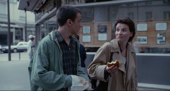 Movie still from “Code Unknown” (2000), directed by Michael Haneke – A man and a woman standing next to each other holding food; Medium shot, Over the shoulder angle