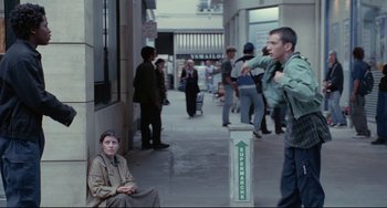Movie still from “Code Unknown” (2000), directed by Michael Haneke – A group of people standing on a sidewalk; Wide shot, Over the shoulder angle