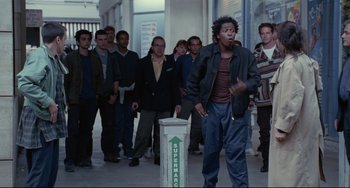 Movie still from “Code Unknown” (2000), directed by Michael Haneke – A group of people standing in a hallway; Wide shot, Over the shoulder angle