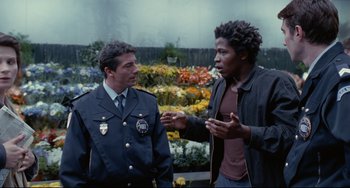 Movie still from “Code Unknown” (2000), directed by Michael Haneke – A man talking to a police officer in uniform; Medium shot, Over the shoulder angle