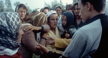 Movie still from “Code Unknown” (2000), directed by Michael Haneke – A group of people standing around each other in the grass; Medium shot, High angle