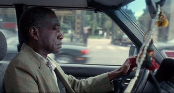 Movie still from “Code Unknown” (2000), directed by Michael Haneke – An older man driving a car on a city street; Medium shot, Over the shoulder angle