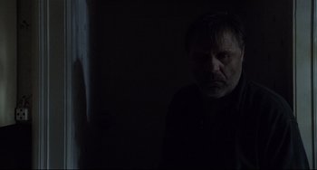 Movie still from “Code Unknown” (2000), directed by Michael Haneke – A man standing in a dark room looking at the camera; Medium shot, Low angle