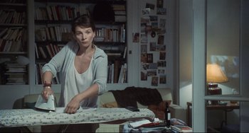 Movie still from “Code Unknown” (2000), directed by Michael Haneke – A woman standing in front of an ironing board in a living room; Medium shot, High angle