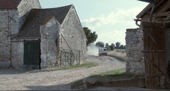 Movie still from “Code Unknown” (2000), directed by Michael Haneke – A truck driving down a dirt road near a stone building; Extreme Wide shot, High angle