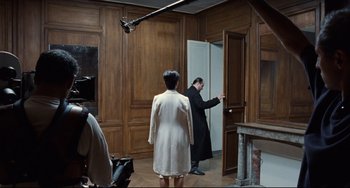 Movie still from “Code Unknown” (2000), directed by Michael Haneke – A man and a woman standing in front of an open door; Wide shot, Over the shoulder angle