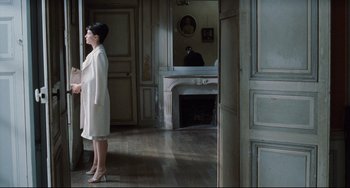 Movie still from “Code Unknown” (2000), directed by Michael Haneke – A woman in a white dress standing in front of a mirror; Wide shot, Over the shoulder angle