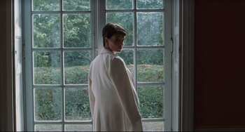 Movie still from “Code Unknown” (2000), directed by Michael Haneke – A woman standing in front of a large window; Medium shot, Low angle