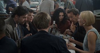 Movie still from “Code Unknown” (2000), directed by Michael Haneke – A group of people sitting around a table eating food; Medium shot, Over the shoulder angle