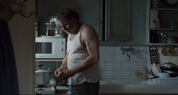 Movie still from “Code Unknown” (2000), directed by Michael Haneke – A man standing in a kitchen preparing a meal; Medium shot, Low angle