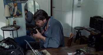 Movie still from “Code Unknown” (2000), directed by Michael Haneke – A man sitting in front of a mirror holding a camera; Medium shot, Over the shoulder angle
