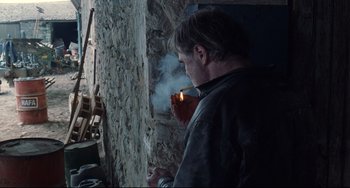 Movie still from “Code Unknown” (2000), directed by Michael Haneke – A man is smoking a cigarette in front of a wall; Medium shot, Over the shoulder angle