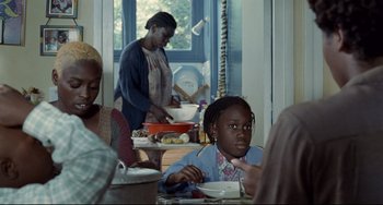 Movie still from “Code Unknown” (2000), directed by Michael Haneke – A group of people sitting at a table eating food; Medium shot, Over the shoulder angle