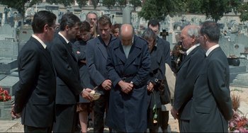 Movie still from “Code Unknown” (2000), directed by Michael Haneke – A group of people standing around each other in front of a grave; Wide shot, High angle