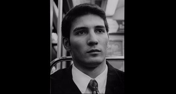 Movie still from “Code Unknown” (2000), directed by Michael Haneke – Black and white photograph of a man in a suit and tie on a bus; Close Up shot, Low angle