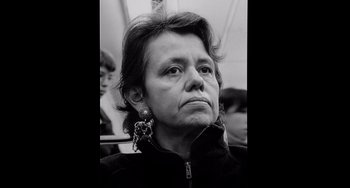 Movie still from “Code Unknown” (2000), directed by Michael Haneke – An older woman wearing a black jacket and a pair of dangling earrings; Close Up shot, Low angle