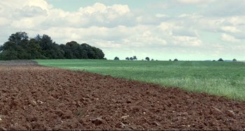 Movie still from “Code Unknown” (2000), directed by Michael Haneke – An open field with green grass and a blue cloudy sky; Extreme Wide shot, High angle