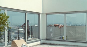 Movie still from “Code Unknown” (2000), directed by Michael Haneke – A man and a woman are relaxing on a balcony; Wide shot, High angle