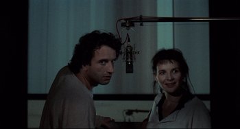 Movie still from “Code Unknown” (2000), directed by Michael Haneke – A man and a woman standing next to each other in front of a microphone; Close Up shot, Over the shoulder angle