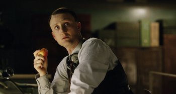 Movie still from “The Death of Stalin” (2017), directed by Armando Iannucci – A man holding an apple while wearing headphones; Close Up shot, Low angle