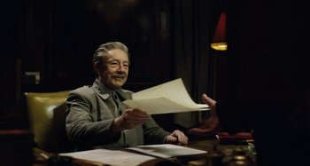 Movie still from “The Death of Stalin” (2017), directed by Armando Iannucci – An older man sitting at a table with papers in front of him; Medium shot, Over the shoulder angle