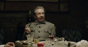 Movie still from “The Death of Stalin” (2017), directed by Armando Iannucci – An older man sitting at a dinner table; Medium shot, Over the shoulder angle