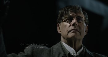 Movie still from “The Death of Stalin” (2017), directed by Armando Iannucci – A person wearing glasses and a jacket; Close Up shot, Over the shoulder angle