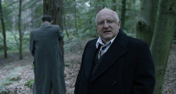 Movie still from “The Death of Stalin” (2017), directed by Armando Iannucci – An older man in a suit and tie standing in front of another man in a suit and tie; Medium shot, Over the shoulder angle