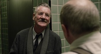 Movie still from “The Death of Stalin” (2017), directed by Armando Iannucci – An older man in a suit looking at himself in the mirror; Close Up shot, Over the shoulder angle