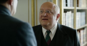 Movie still from “The Death of Stalin” (2017), directed by Armando Iannucci – An older man wearing a suit and tie; Close Up shot, Over the shoulder angle