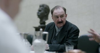 Movie still from “The Death of Stalin” (2017), directed by Armando Iannucci – An older man sitting in front of a bust; Close Up shot, Over the shoulder angle