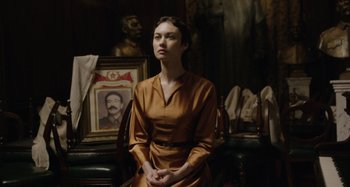 A woman sitting in front of a portrait of a man