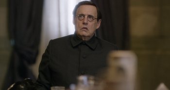 Movie still from “The Death of Stalin” (2017), directed by Armando Iannucci – A man in a black suit sitting in front of a table; Close Up shot, Over the shoulder angle