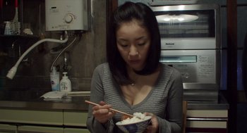 Movie still from “Cold Fish” (2010), directed by Sion Sono – A woman holding chopsticks while eating a bowl of food; Close Up shot, High angle