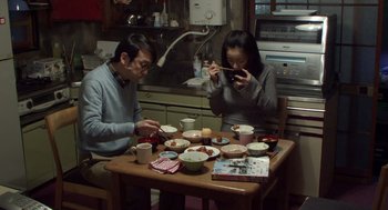 Movie still from “Cold Fish” (2010), directed by Sion Sono – A man and a woman sitting at a dinner table; Medium shot, High angle