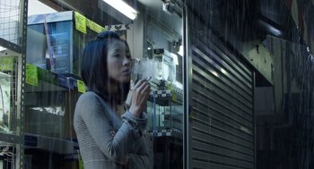 Movie still from “Cold Fish” (2010), directed by Sion Sono – A woman smoking a cigarette in front of a store window; Medium shot, Low angle