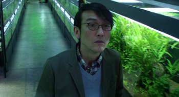 Movie still from “Cold Fish” (2010), directed by Sion Sono – A man in a jacket and a plaid tie; Close Up shot, Low angle