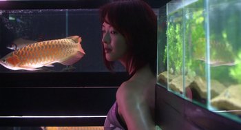 Movie still from “Cold Fish” (2010), directed by Sion Sono – A woman standing in front of a fish in a tank; Medium shot, Low angle
