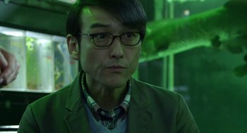 Movie still from “Cold Fish” (2010), directed by Sion Sono – A person wearing glasses and a suit jacket; Close Up shot, Low angle
