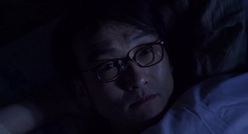 Movie still from “Cold Fish” (2010), directed by Sion Sono – A man with glasses is looking at the camera; Close Up shot, Low angle