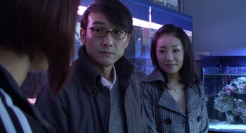 Movie still from “Cold Fish” (2010), directed by Sion Sono – A man and a woman standing next to each other in front of a building; Close Up shot, Over the shoulder angle