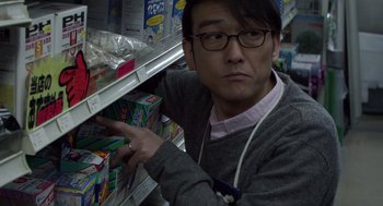 Movie still from “Cold Fish” (2010), directed by Sion Sono – A man in glasses and a hat is looking at a shelf of cereal; Close Up shot, Over the shoulder angle