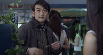 Movie still from “Cold Fish” (2010), directed by Sion Sono – A man standing in front of a group of people; Medium shot, Over the shoulder angle