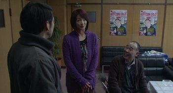 Movie still from “Cold Fish” (2010), directed by Sion Sono – A woman standing next to two other people; Medium shot, Over the shoulder angle