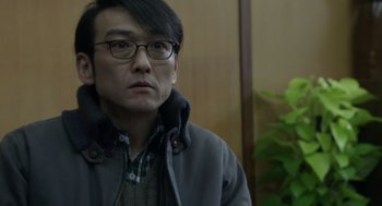Movie still from “Cold Fish” (2010), directed by Sion Sono – A man wearing glasses and a jacket looking to his left; Close Up shot, Over the shoulder angle