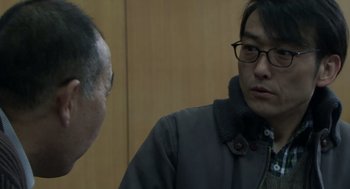 Movie still from “Cold Fish” (2010), directed by Sion Sono – A man wearing glasses talking to another man in a room; Close Up shot, Over the shoulder angle